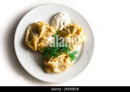 Fried asian dumplings Gyozas Or Russian, Ukrainian dumplings, potstickers in white ceramic plate served with sour cream. Close up. Asian dinner. Flat lay. White isolated background. Copy Space.  Stock Photo