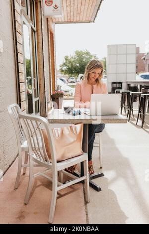 Young female professional works outside coffee shop on laptop computer Stock Photo
