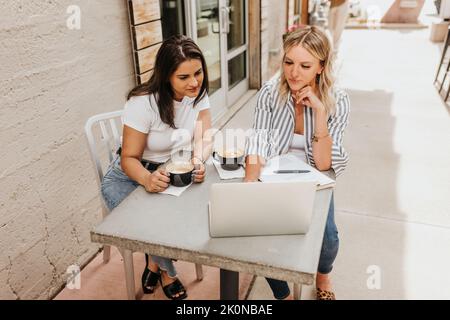 Two professional females work on computer together over coffee Stock Photo