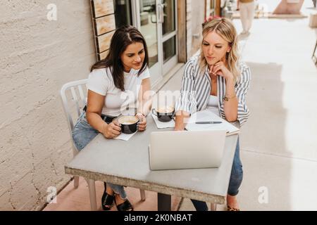 Two young female professionals work outside on laptop together Stock Photo