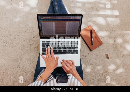 Young professional female types on laptop computer sitting outside Stock Photo
