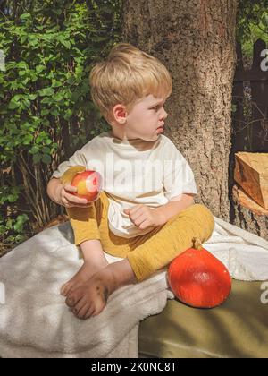 A child sits on a suitcase, a pumpkin and an apple, barefoot Stock Photo