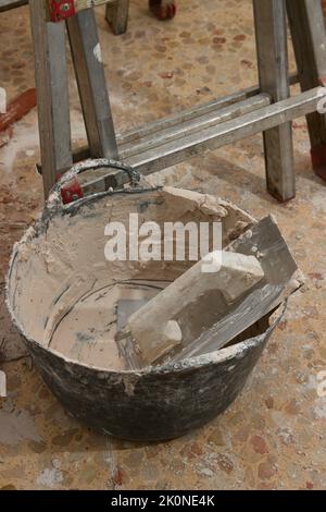 Close-up of the tools of a bricklayer who is repairing the interior of a house, we see a trowel, a carrycot with plaster and a ladder Stock Photo