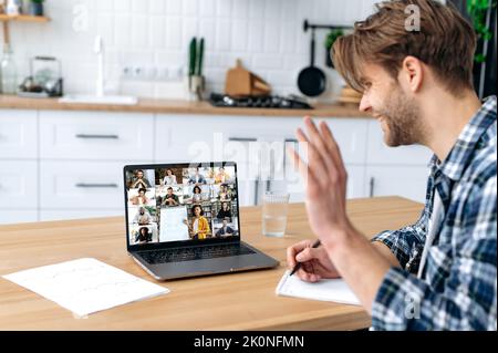 Online lesson, distance education. Side view of a smart caucasian male student and group of multiracial people on a laptop screen. Clever guy listening to an online lecture, webinar, gain knowledge Stock Photo