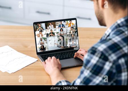 Successful caucasian guy sitting in kitchen at home talking by video conference with group of multiracial successful colleagues discuss company promotion, holding online brainstorm about new project Stock Photo