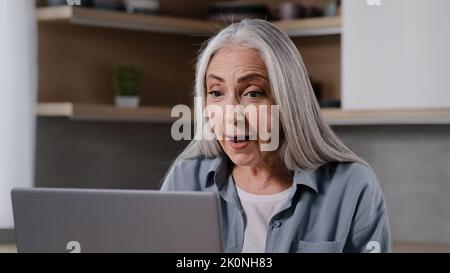 Caucasian mature middle-aged female pensioner woman chatting online distance communication remote with family children during quarantine looking at Stock Photo
