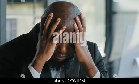 Sick exhausted african man suffer from headache migraine syndrome hold head by hands tired overworked american adult disappointed unhealthy Stock Photo