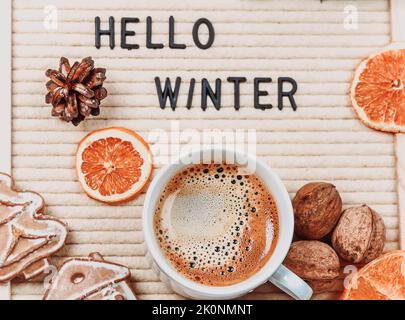 Lettering hello winter on letter board. Fir branches, dried oranges, nuts and a cup of coffee. minimalistic new year background 2023 Stock Photo