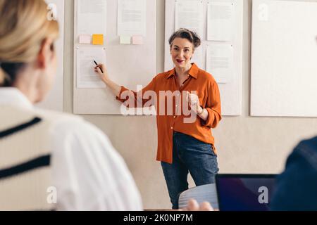 Mature businesswoman giving a presentation to her team during a meeting. Happy team leader discussing marketing reports with her colleagues. Group of Stock Photo