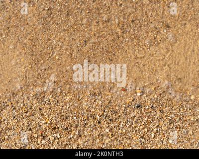 Sand texture on a bathing beach. Clear transparent water with air bubbles is visible. Top down view with fine small stones. Abstract background. Stock Photo