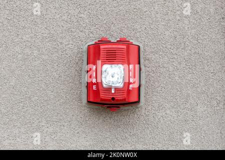 Red fire alarm siren with flashing light strobe isolated on gray cement wall outdoor. Fire safety Stock Photo