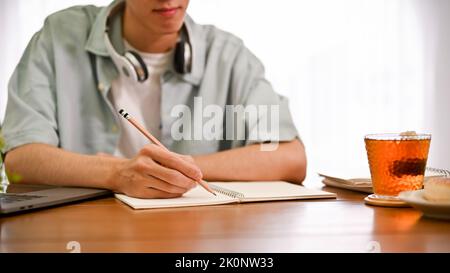 Smart young Asian male college student doing his homework, writing something on his diary. cropped image Stock Photo