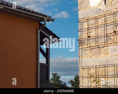 Old wall with a grid for climbing plants. The renovated building exterior is lit by sunlight. Another building and a blue sky are in the background. Stock Photo