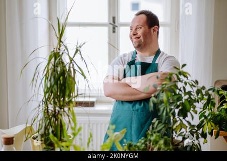 Young man with Down syndrome taking care of plants, working in fowershop. Stock Photo