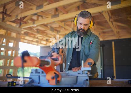 Construction worker working with eletric saw inside wooden construction of house, diy eco-friendly homes concept. Stock Photo