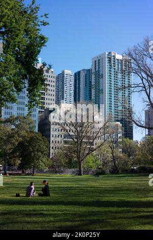 Couple sit on the grass in Melbourne's Flagstaff Gardens with the city skyline beyond. Stock Photo
