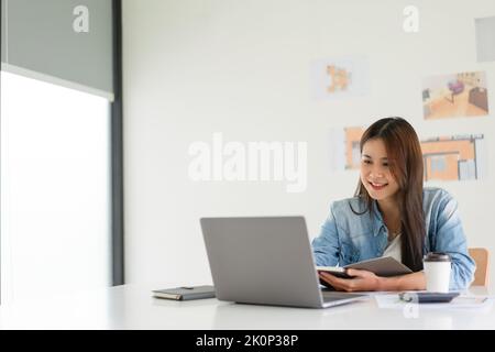 Construction design concept, Female architect taking notes while working about house plan on laptop. Stock Photo