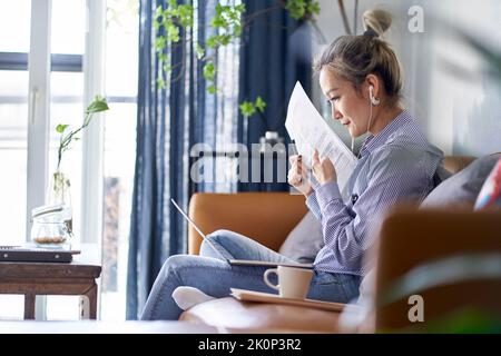 mature professional asian woman working from home showing a paper document during online video meeting Stock Photo