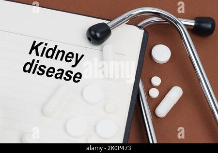 Medical concept. On a brown surface lies a stethoscope, pills and a notepad with the inscription - Kidney disease Stock Photo