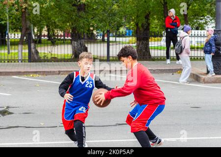 Team in colorful uniforms,Cute two young boys playing basketball game on street playground Tomsk Russia September 10, 2022.Sports Education,selective Stock Photo