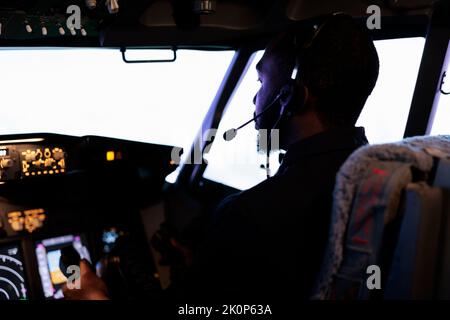 African american copilot holding lever to takeoff with airplane, flying aircraft with dashboard power buttons and control panel command. Radar navigation and windscreen compass. Close up. Stock Photo