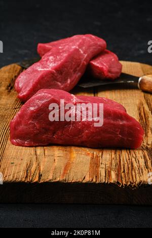 Closeup view of raw beef steak chopped on slices on shabby cutting board Stock Photo