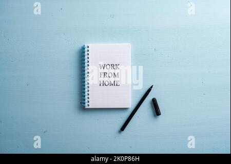 Open spiral notebook with a Work from home sign written in it and a blue marker next to it. Over pastel blue wooden background. Stock Photo