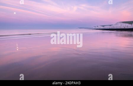 Purple morning blue hour and September full moon setting during low tide at Birling Gap and the Seven sisters on the east Sussex coast south east Engl Stock Photo
