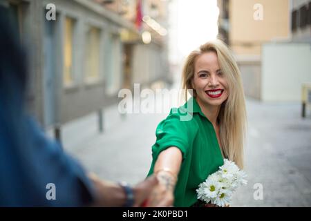 Selective focus on a happy blonde woman holding hands with an african man in the street Stock Photo