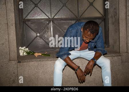 Sad african man sitting in the street beside a bunch of flowers at night Stock Photo