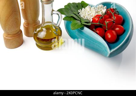 Spinach, cottage cheese, tomatoes in a heart shaped bowl and olive oil with spices isolated on white background with copy space. selective focus Stock Photo