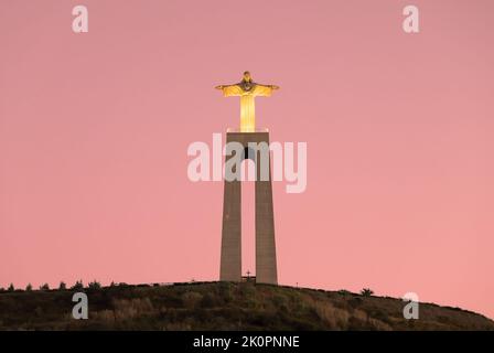 Christ the King, Cristo Rei statue in Almada, Lisbon, Portugal. The illuminated Jesus Christ monument as seen from Tagus river during sunset. Stock Photo