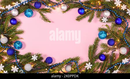 Creative vibrant Christmas frame with fir branches and blue and silver ornaments on pastel pink background. Flat lay copy space Stock Photo