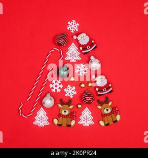 Creative Christmas tree shape made with various ornaments on red background. Flat lay Stock Photo