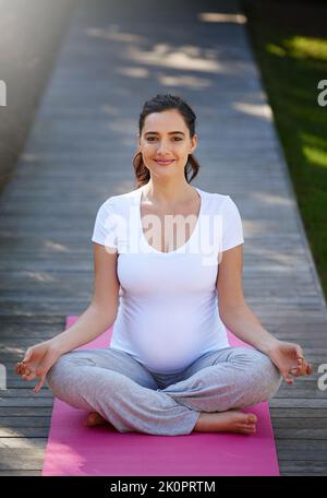 Staying healthy and happy through yoga. Portrait of a young pregnant woman doing yoga outside. Stock Photo