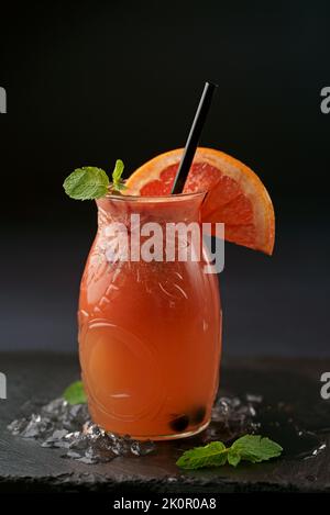 Grapefruit juice in a glass jar with pieces of fruit on a wooden table, selective focus Stock Photo