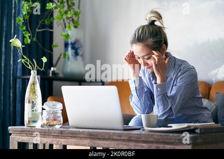 mature professional asian business woman working from home appearing to be tired and exhausted Stock Photo