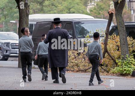 An orthodox Jewish father & his 3 identically dressed children walk in Williamsburg, Brooklyn on a mild late summer 2022 day. Stock Photo