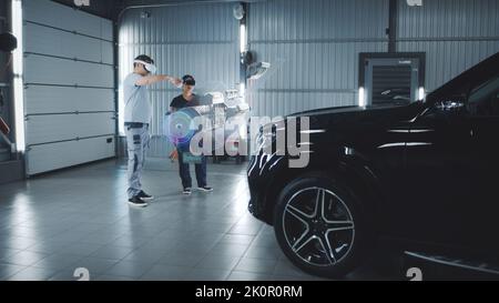 Two technicians check a car engine using virtual reality technology in a workshop. Experts discuss the characteristics of the motor of the car, its components and parts Stock Photo
