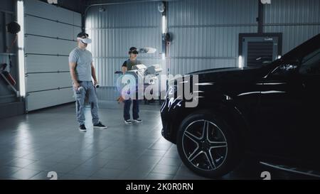 Two technicians check a car engine using virtual reality technology in a workshop. Experts discuss the characteristics of the motor of the car, its components and parts Stock Photo