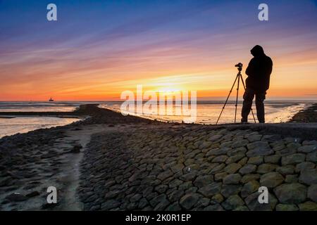 Tourist with camera during sunset on the Tischendamm, North Sea at low tide, on the left the Mittelplate oil drilling platform
