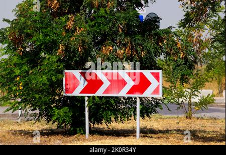 Turn road traffic direction white arrows red background sign in front of a tree Stock Photo