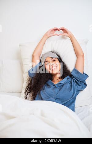 A beautiful young multi-ethnic woman makes heart shape with hands waking up Stock Photo