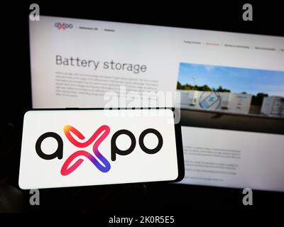 Person holding smartphone with logo of Swiss energy company Axpo Holding AG on screen in front of website. Focus on phone display. Stock Photo