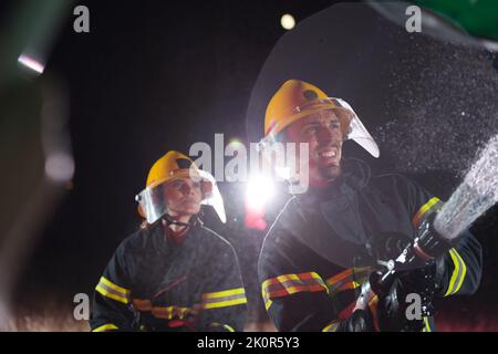 Firefighters using a water hose to eliminate a fire hazard. Team of female and male firemen in dangerous rescue mission.  Stock Photo