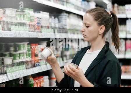 a young lady in the store chooses yogurt products, reads and compares the composition on the labels. The concept of healthy eating low-fat foods. Stock Photo