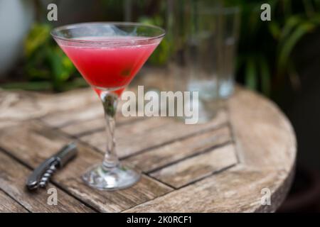 red cocktail with ice in glass with stem on wooden surface Stock Photo