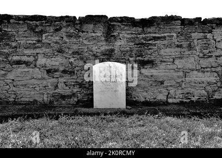 A grayscale shot of tombstone against the stone fence in Italian cemetery Stock Photo