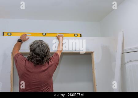 An employee checks the level of drywall before painting it using a level to ensure that the walls are equal Stock Photo