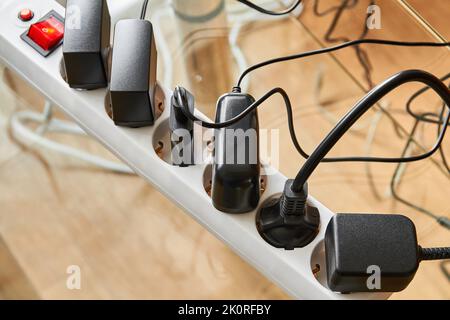 Electrical power strip overloaded with multiple electrical cords plugged in. Many plugs plugged into electric power bar Stock Photo